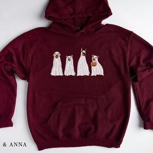 May include: Burgundy hooded sweatshirt featuring a graphic of four dogs dressed as ghosts for Halloween. The dogs are wearing white ghost costumes with their heads poking out. One dog is holding a small orange pumpkin.