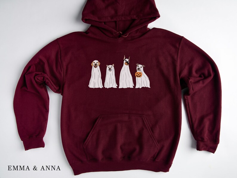 May include: Burgundy hooded sweatshirt featuring a graphic of four dogs dressed as ghosts for Halloween. The dogs are wearing white ghost costumes with their heads poking out. One dog is holding a small orange pumpkin.