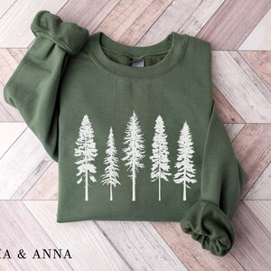 May include: A green sweatshirt with a white silhouette of five pine trees printed on the front.