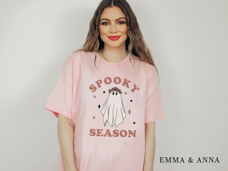 May include: Pink t-shirt with a white ghost wearing a floral crown and the text "Spooky Season" in brown lettering.