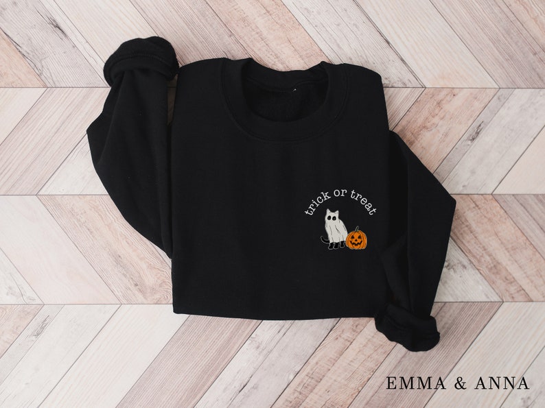 May include: Black sweatshirt with a white ghost cat and pumpkin design and the text "trick or treat".