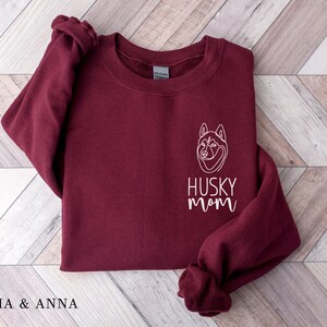 Pode incluir: Camisola de cor bord&ocirc; com um contorno branco de um c&atilde;o husky e o texto "Husky Mom" na frente.