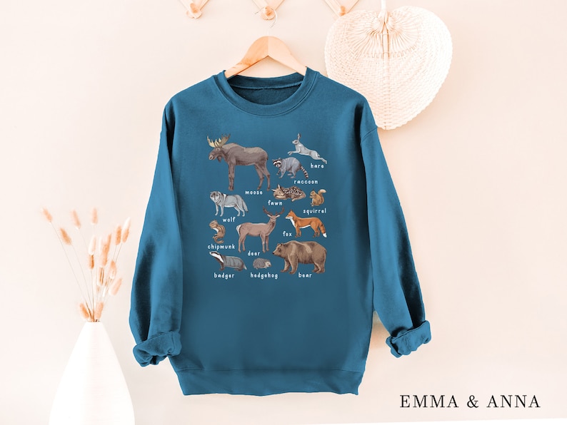 May include: A teal blue sweatshirt with a graphic print of various forest animals, including a moose, wolf, deer, fox, bear, raccoon, squirrel, chipmunk, badger, and hedgehog. The animals are labeled with their names.