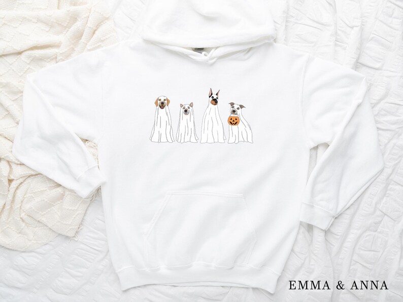 May include: White hoodie featuring a graphic of four dogs dressed as ghosts for Halloween. The dogs are a Labrador Retriever, a Beagle, a Doberman Pinscher, and a Jack Russell Terrier. The text "EMMA & ANNA" is printed on the bottom right corner of the hoodie.