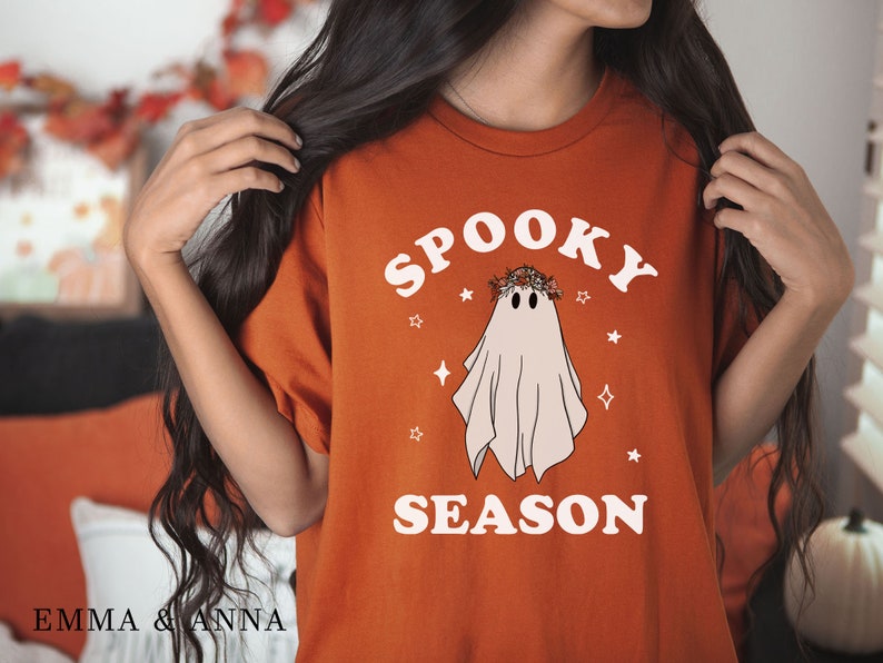 May include: A burnt orange t-shirt with a white graphic of a ghost wearing a flower crown and the text "Spooky Season".