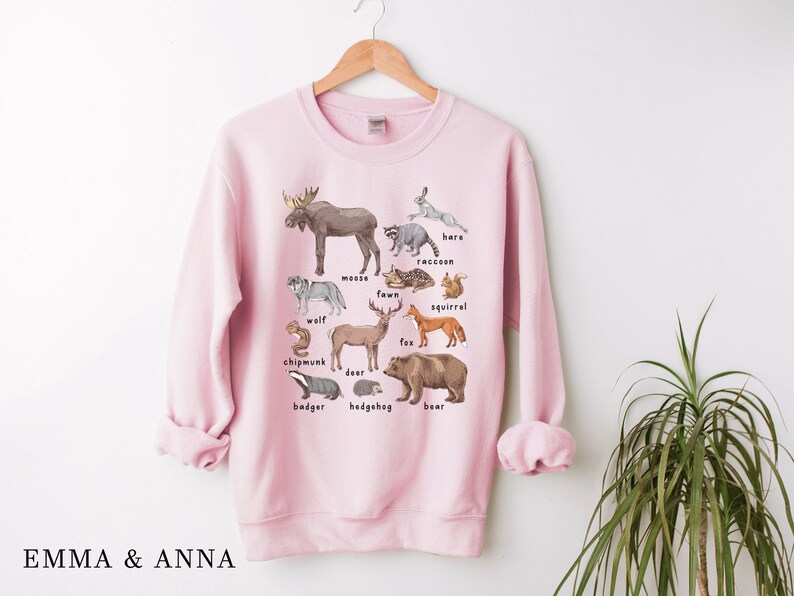 May include: Pink sweatshirt with a graphic print of various woodland animals, including a moose, deer, fox, squirrel, raccoon, badger, hedgehog, and bear. The animals are labeled with their names.