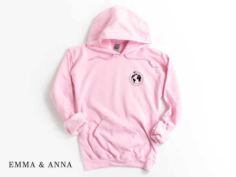 May include: Pink hoodie with a black globe and airplane graphic on the front. The hoodie has a drawstring hood and a kangaroo pocket.
