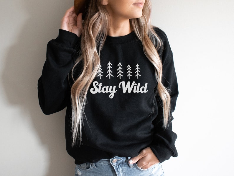 K&ouml;nnte beinhalten: Schwarzer Pullover mit einem wei&szlig;en Aufdruck einer Reihe von Kiefern und dem Text "Stay Wild".