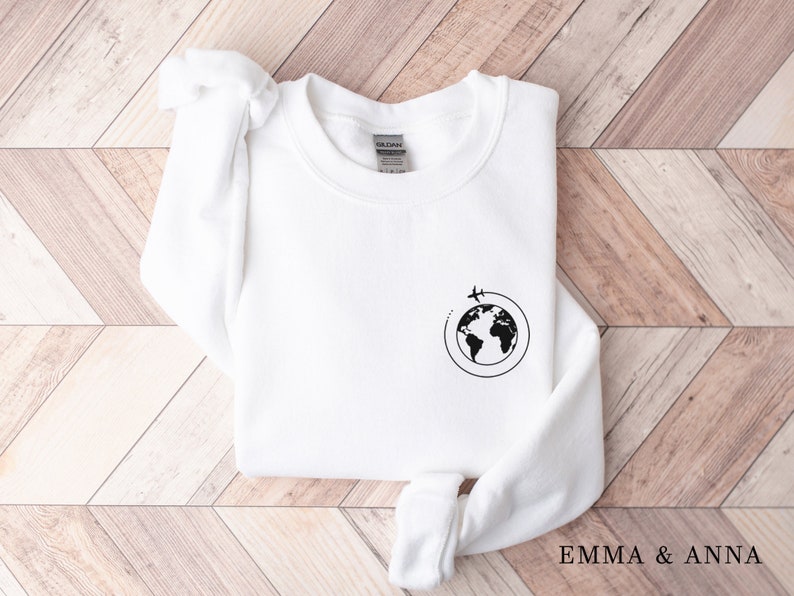 May include: White sweatshirt with a black graphic of a globe with airplanes flying around it. The text "EMMA & ANNA" is printed on the bottom right corner of the image.