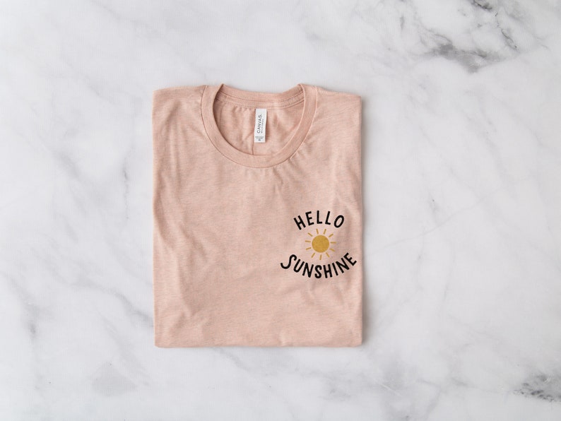 May include: A folded pink t-shirt with a black graphic that says "Hello Sunshine" with a yellow sun graphic.
