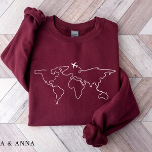 May include: Burgundy sweatshirt with a white outline of the world map and a small airplane graphic.