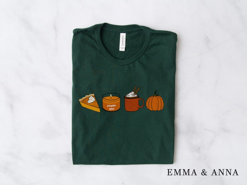 May include: A dark green t-shirt with a graphic of a pumpkin spice candle, a slice of pumpkin pie, a pumpkin, and a cup of pumpkin spice latte.