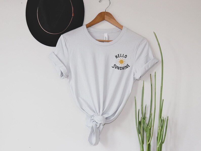 May include: A light gray t-shirt with a graphic of a sun and the text "Hello Sunshine" on the front.