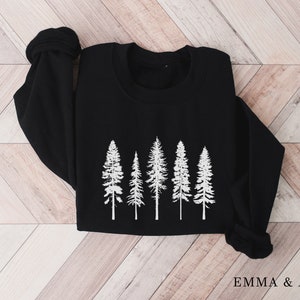 May include: Black sweatshirt with a white graphic of five pine trees. The text "EMMA & ANNA" is printed on the bottom right corner of the sweatshirt.