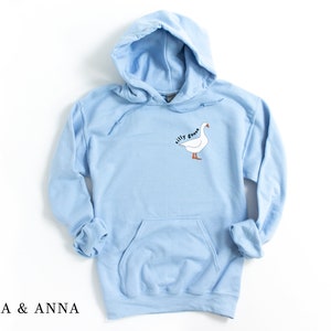 K&ouml;nnte beinhalten: Ein hellblauer Kapuzenpullover mit einem wei&szlig;en G&auml;nse-Motiv und dem Text "silly goose" auf der Vorderseite.