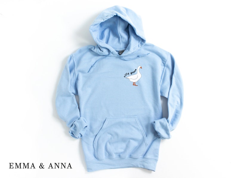 K&ouml;nnte beinhalten: Ein hellblauer Kapuzenpullover mit einem wei&szlig;en G&auml;nse-Motiv und dem Text "silly goose" auf der Vorderseite.