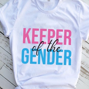 May include: White t-shirt with the text "KEEPER of the GENDER" in pink and blue lettering.