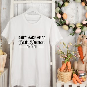 May include: White t-shirt with black text that reads "Don't make me go Beth Dutton on you".