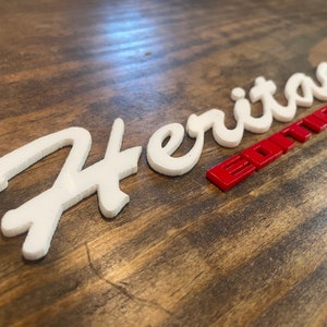 May include: White "Heritage" lettering with a red "Edition" label on a wooden surface.