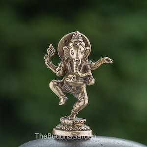May include: A small, gold-colored brass statue of the Hindu deity Ganesha. The statue depicts Ganesha in a dancing pose, with his trunk raised and his hands in a gesture of blessing. The statue is set on a small, circular base.