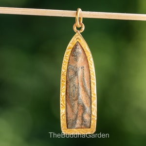 May include: A gold pendant with a detailed, ornate frame. The pendant features a brown and gray image of a standing Buddha.