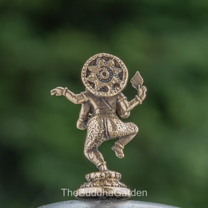 May include: A small, gold-colored statue of a deity with a circular headpiece and a raised arm holding a weapon. The statue is standing on a small base.