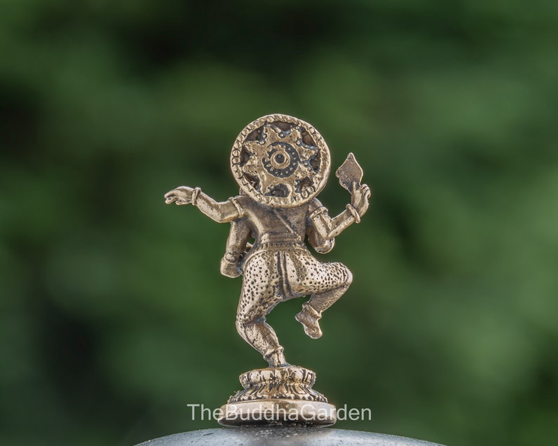 May include: A small, gold-colored statue of a deity with a circular headpiece and a raised arm holding a weapon. The statue is standing on a small base.
