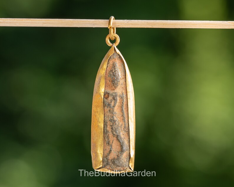 May include: A gold-plated pendant featuring a brown and gray Buddha image. The pendant is shaped like a teardrop and has a loop at the top for attaching a chain.