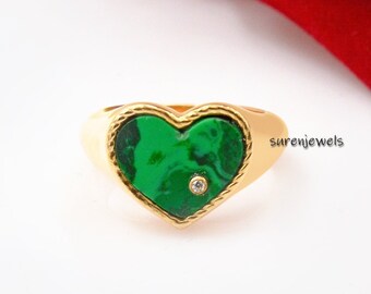 May include: Gold heart-shaped ring with a green stone and a small diamond accent. The ring is on a white background.