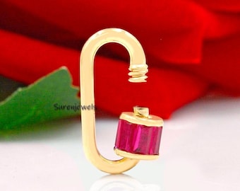 May include: Gold charm with a red cubic zirconia stone. The charm is shaped like a carabiner clip.