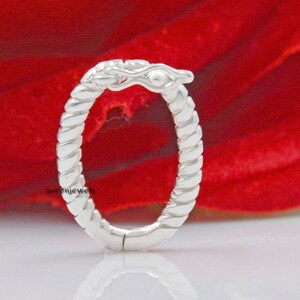 May include: A silver oval hoop earring with a twisted rope design. The hoop is open and has a small, decorative detail at the top.