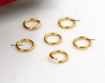 Könnte beinhalten: Sechs goldfarbene Sprungringe, auch Verbindungsringe genannt, liegen auf einer weißen Oberfläche. Die Ringe sind klein und rund, perfekt für die Schmuckherstellung oder das Basteln.