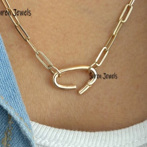 May include: A gold chain necklace with a unique oval-shaped clasp. The chain is made of small, linked rectangles.