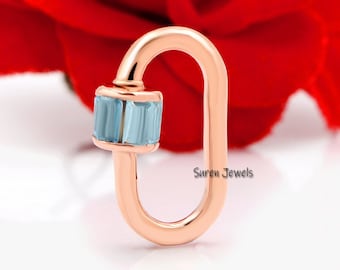 May include: Rose gold charm with a light blue gemstone. The charm is shaped like a figure eight and has a small loop at the top. The charm is on a white background.