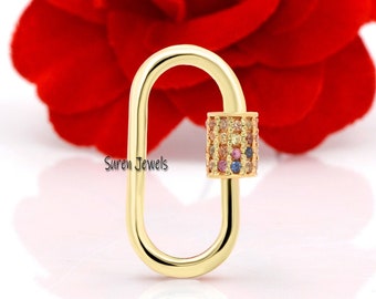 May include: Gold-toned oval-shaped clasp with a small, colourful, cubic zirconia-encrusted cylinder on one side. The clasp is photographed against a red rose.