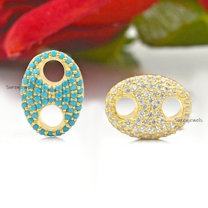 Op de afbeelding: Twee gouden ovale connector charms met een dubbel lusontwerp. Een charme is bezet met turquoise stenen en de andere met heldere stenen.