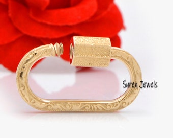 May include: Gold-toned metal clasp with an ornate design. The clasp is open and ready to be attached to a chain or other jewelry.