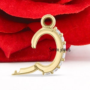 May include: A gold charm in the shape of the letter C, with a small keyhole detail. The charm is decorated with small, clear cubic zirconia stones.