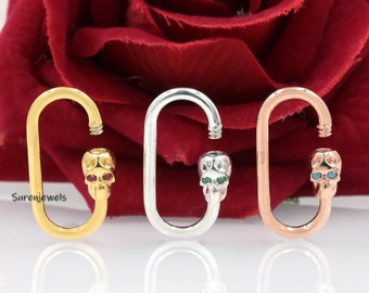 May include: Three oval-shaped skull charm connectors in gold, silver, and rose gold. Each charm features a skull with green and red gemstone eyes.