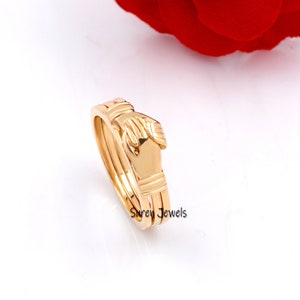 May include: Gold-toned interlocking hands ring. The ring is made of two bands that are intertwined to form the shape of two hands clasped together. The ring is a symbol of love, friendship, and unity.