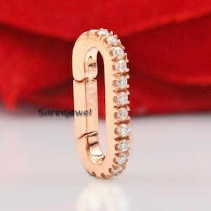 May include: A rose gold oval-shaped charm with a row of clear cubic zirconia stones around the edge. The charm has a clasp closure.