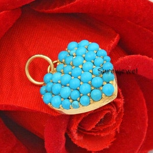 May include: A gold heart-shaped charm with a turquoise stone inlay. The charm is on a red velvet background.