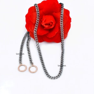 Puede incluir: Un collar de cadena de plata con dos pequeños anillos de oro rosa unidos. La cadena está sobre una rosa roja.