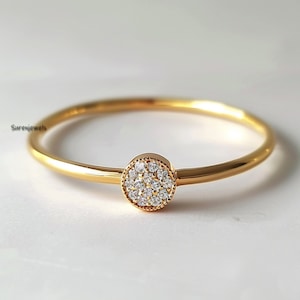 Może przedstawiać: Złota bransoletka typu bangle z okrągłym, diamentowym centrum w stylu pavé. Bransoletka jest prosta i elegancka.