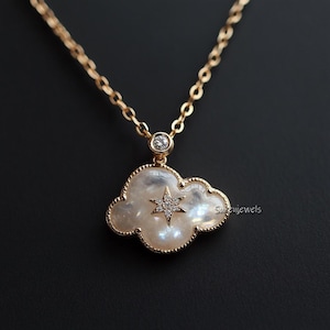 Könnte beinhalten: Eine goldene Kettenkette mit einem weißen Perlmutt-Wolkenanhänger, der einen Stern mit kleinen Diamanten zeigt. Der Anhänger ist mit einem kleinen runden Diamanten verziert.