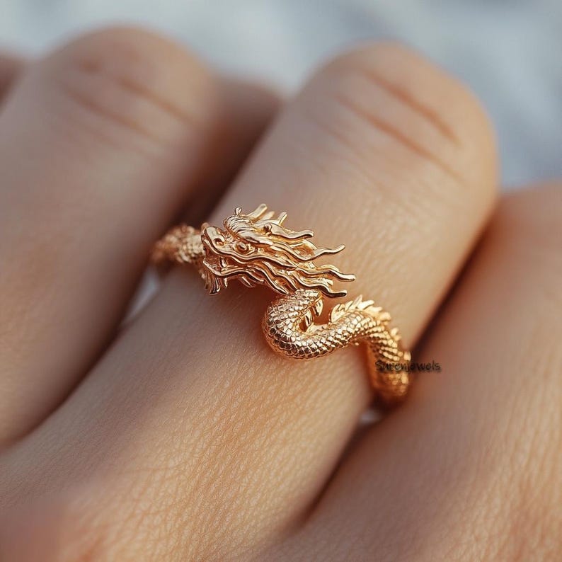 Puede incluir: Un anillo de drag&oacute;n dorado con un dise&ntilde;o detallado. La cabeza del drag&oacute;n est&aacute; mirando hacia adelante con la boca abierta y las alas extendidas. El anillo se lleva en un dedo.