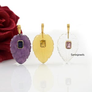 May include: Three gold leaf pendants with different colored gemstones. The pendants are made of amethyst, citrine, and clear quartz. Each pendant features a small square gemstone in the center.