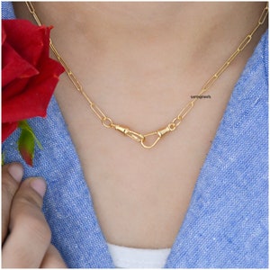 Op de afbeelding: Een gouden ketting met een uniek sluitingontwerp. De ketting is gemaakt van kleine, met elkaar verbonden ovalen. De sluiting is gemaakt van twee in elkaar grijpende lussen.
