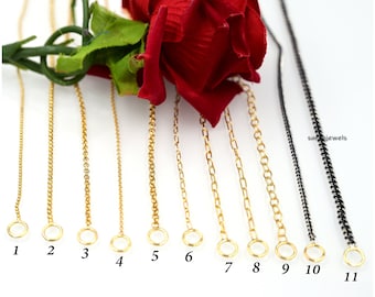 May include: Eleven gold and one black chain necklaces of varying lengths and styles. The chains are numbered 1 through 11. The chains are laid out on a white surface with a red rose in the background.