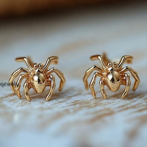 May include: A pair of gold-toned spider earrings. The spiders are detailed and have eight legs.